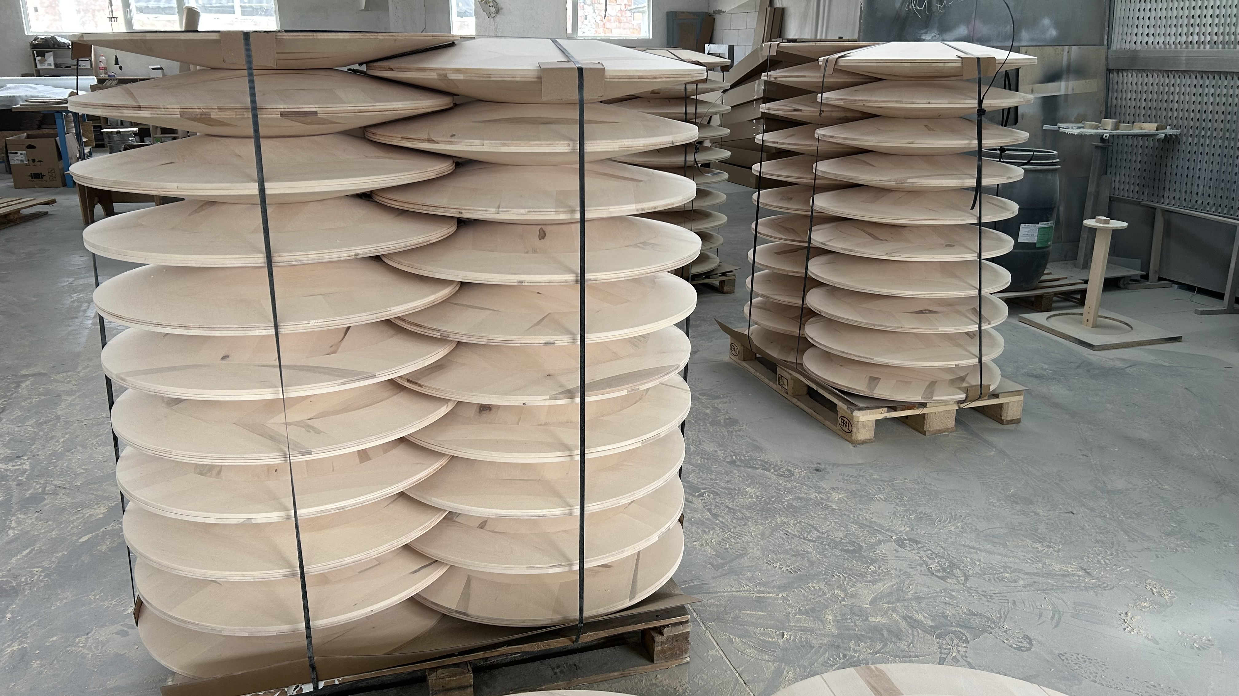 Large batch of solid wood round table tops stacked on pallets in production facility